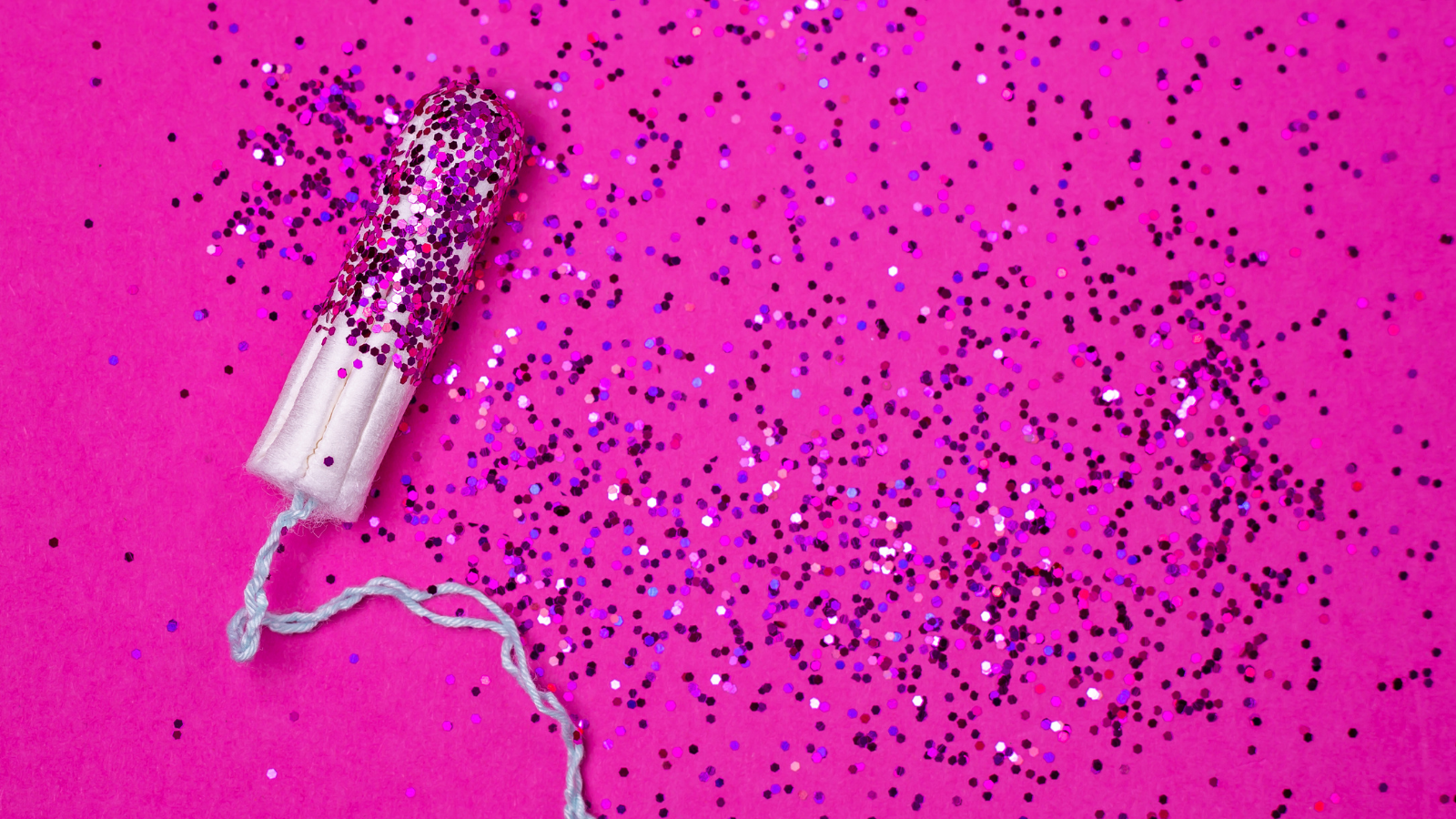 Periods don't pause for pandemics. Image of a tampon lying on lots of pink glitter