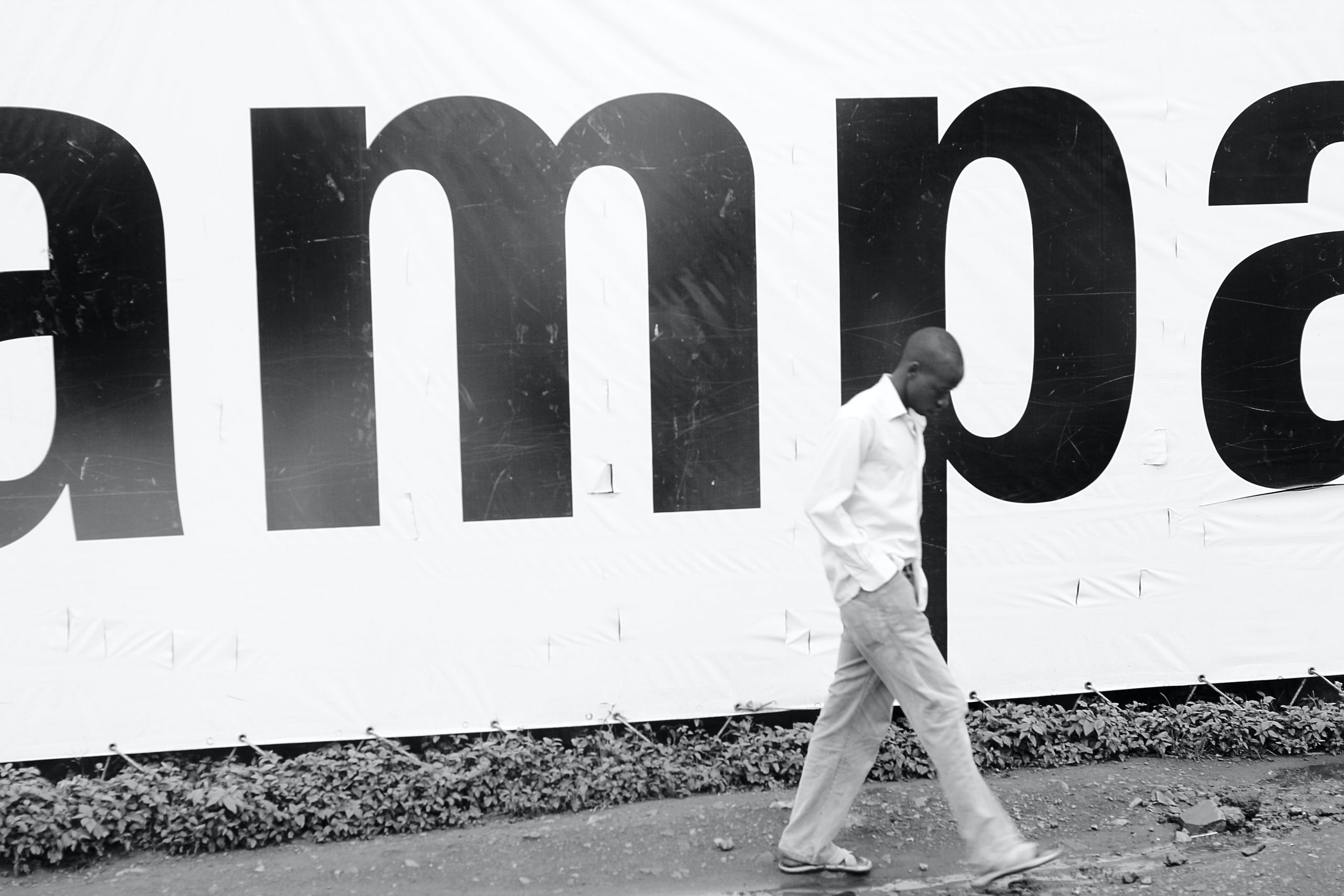 Man walks in front of a Kampala sign